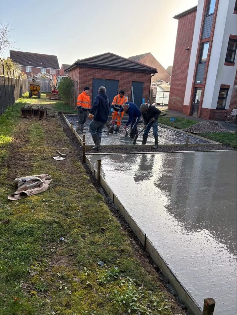 A group of men pour and level concrete for the base of the shed